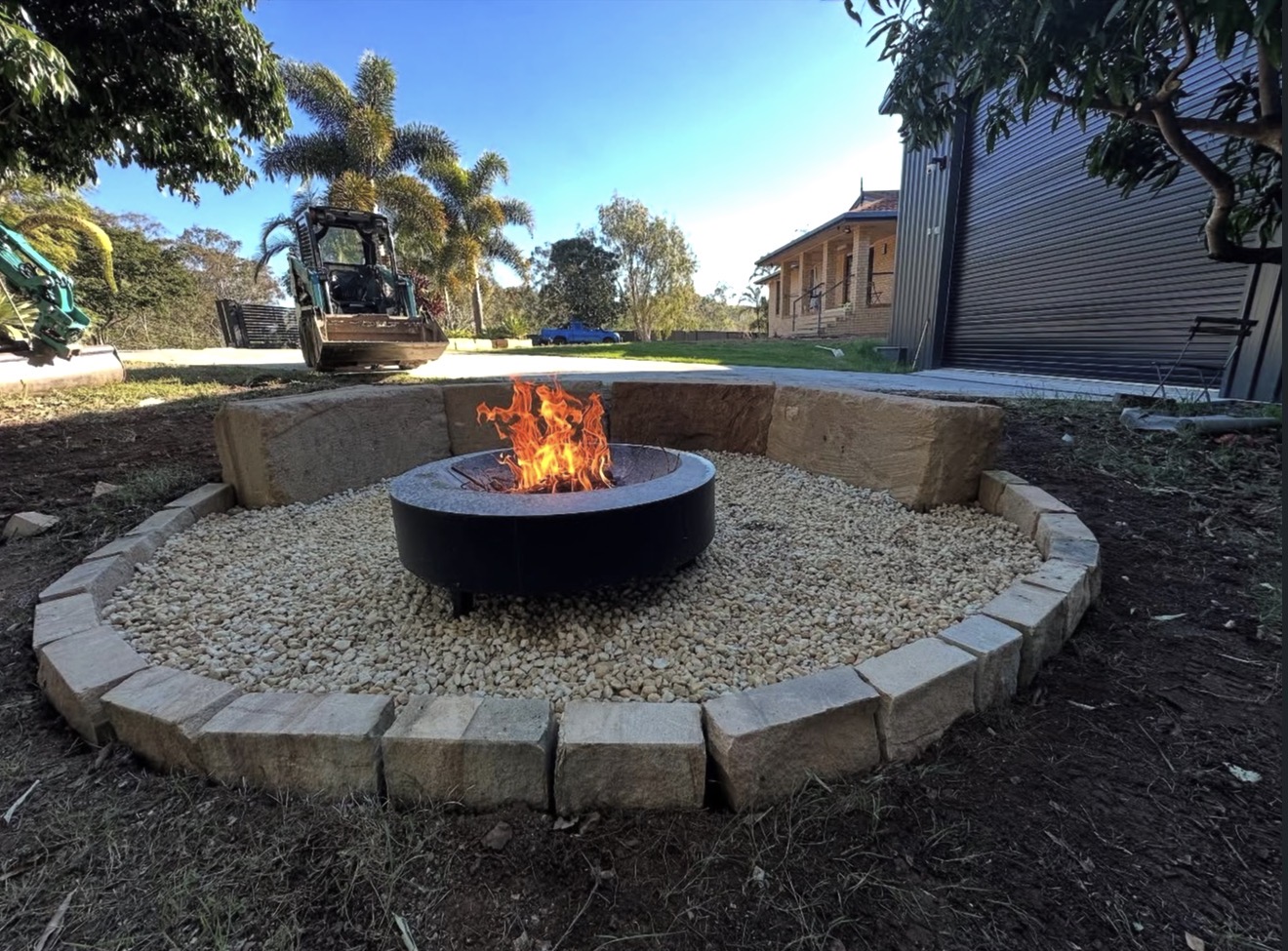 Circular outdoor fire pit set within sandstone block bench seating and gravel surround